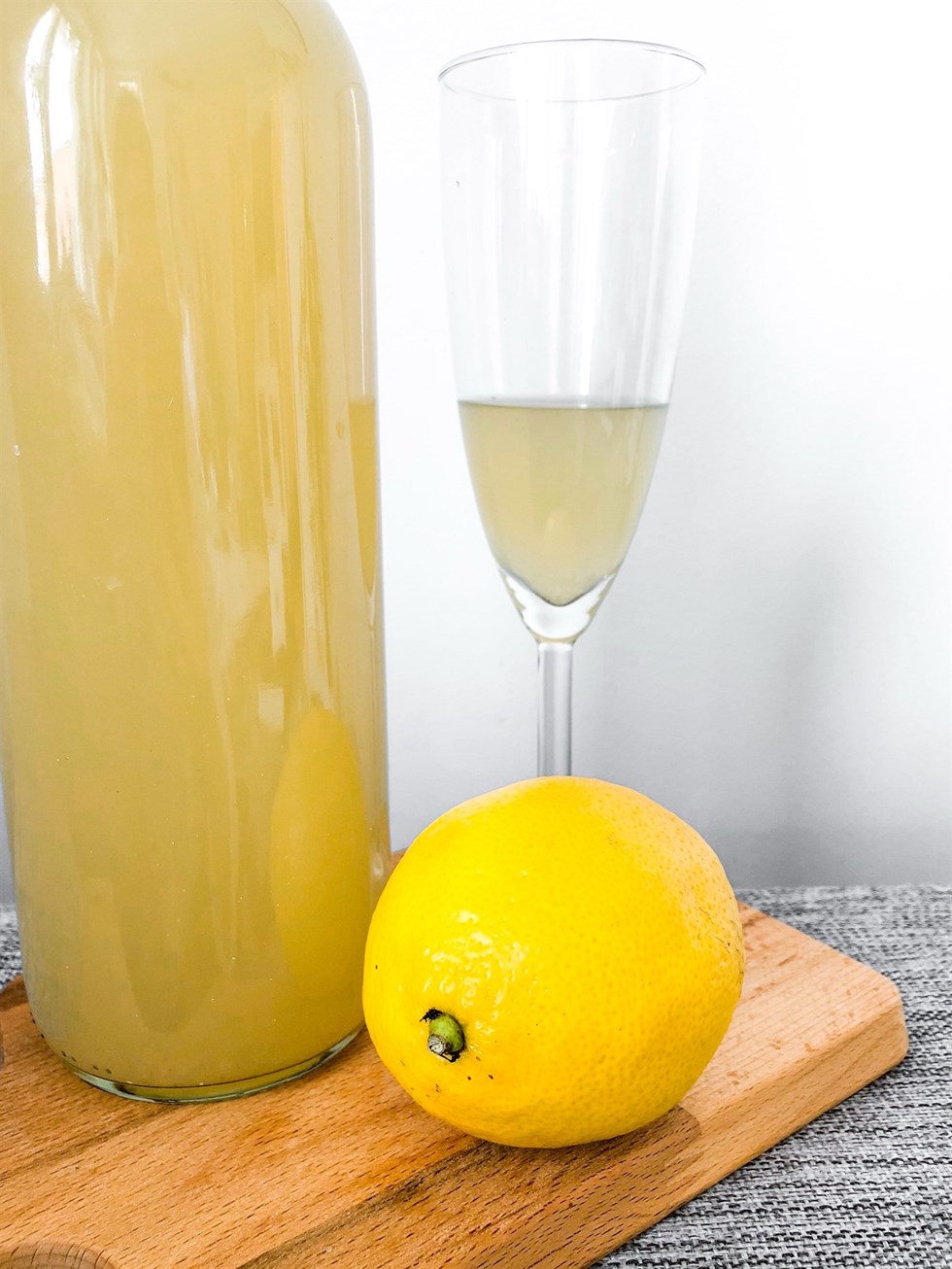 Flaska och glas med ingefärsshot bredvid en färsk citron på en skärbräda.