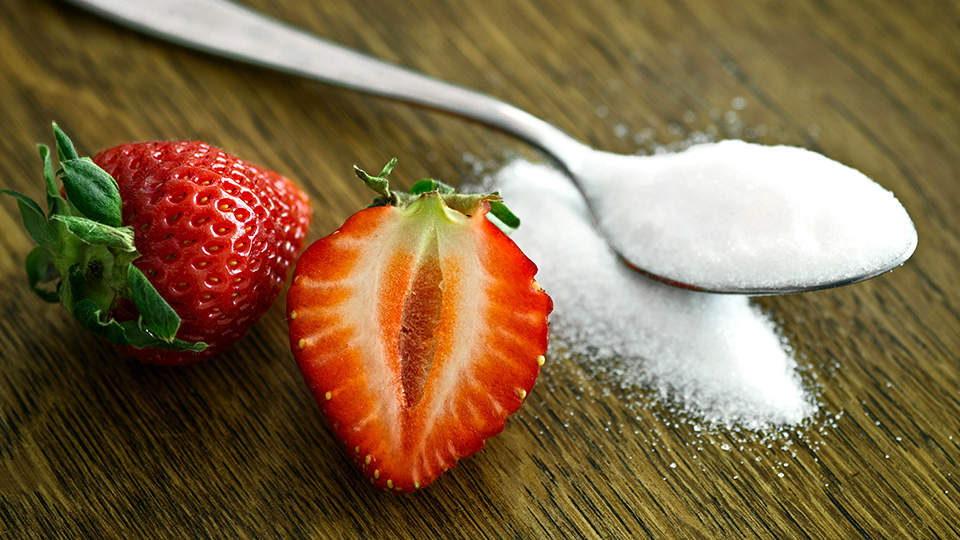 Jordgubbe skuren i halvor bredvid sockersked